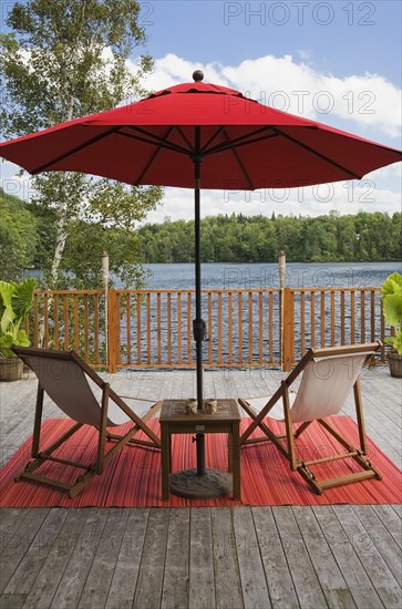 Red canvas cloth parasol and wooden folding canvas chairs on red mat on grey wood plank deck with
