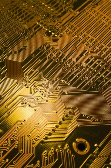 Close-up of golden yellow lighted electronic computer circuit board with lines and silver solder