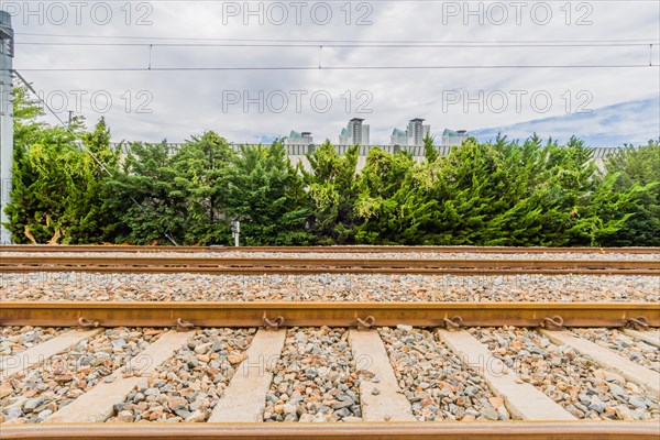 Railway tracks on a bright day with lush green foliage and city buildings under a sky with fluffy