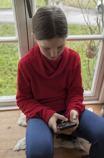 Girl, 10 years old, sitting on the windowsill with mobile phone, Mecklenburg-Vorpommern, Germany,