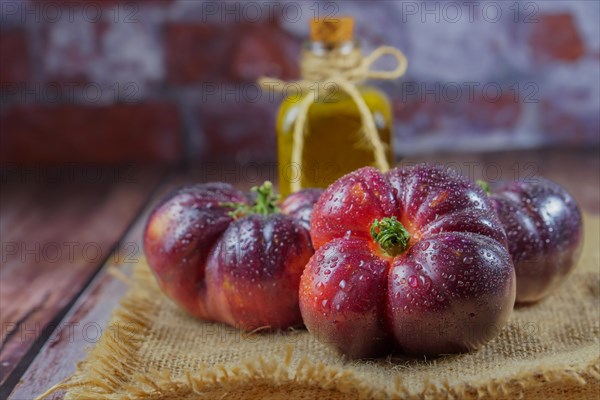 Group of tasty fresh tomatoes of the blue variety on a burlap cloth with a bottle of olive oil in