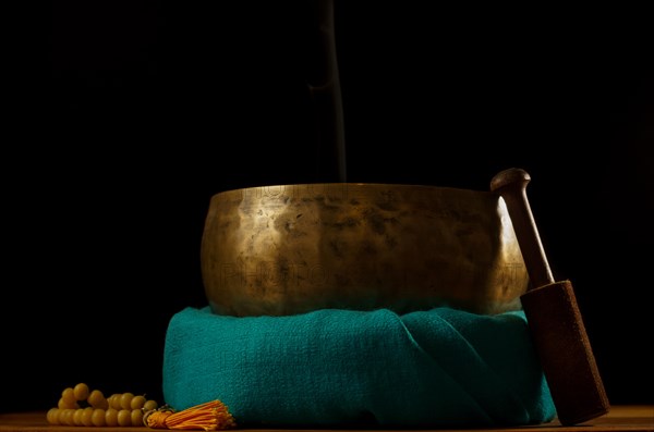 Tibetan singing bowl smoking on green cloth next to a Buddhist japa mala isolated on black
