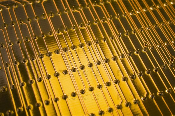 Close-up of golden yellow lighted electronic computer circuit board with lines and silver solder