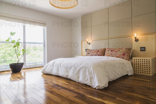 King size bed covered with white bedspread in bedroom with American walnut hardwood flooring on