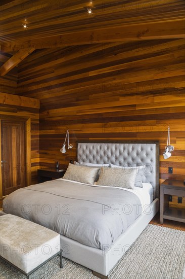 King size bed with grey upholstered panel headboard, ottoman and wooden end tables in master