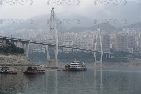 Chongqing, Chongqing Province, Modern bridge over a river with light fog, cityscape behind,