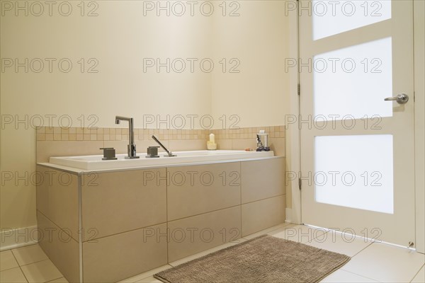 Soaking tub encased in a ceramic tile base in bathroom inside a renovated ground floor apartment in