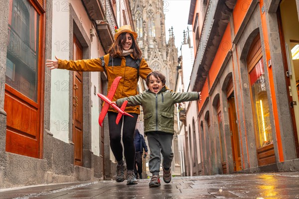 A woman and a child are playing with a red kite in a narrow alleyway. The scene is lively and
