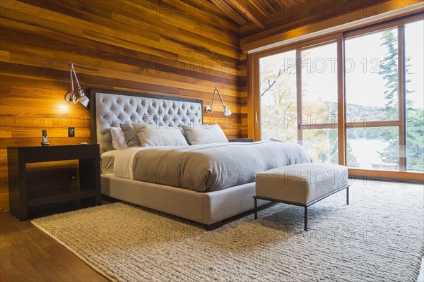King size bed with grey upholstered panel headboard, ottoman and wooden end tables in master