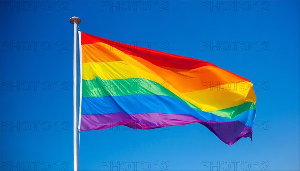 The rainbow flag flutters in the wind, isolated, against the blue sky. In many cultures around the