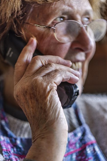 Laughing senior citizen with smock talking on the phone at home in her living room, Cologne, North