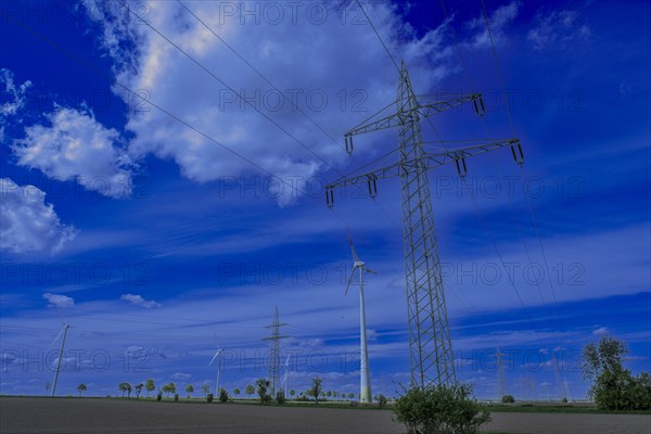 Power pylons with high-voltage lines and wind turbines on the K63 road with trees at the Avacon