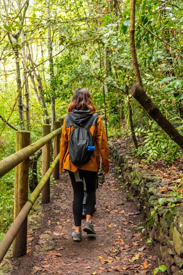 A woman is walking down a path in the woods, wearing a yellow jacket and carrying a backpack