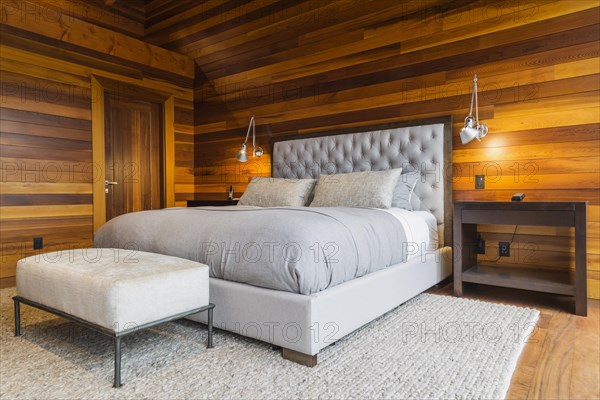 King size bed with grey upholstered panel headboard, ottoman and wooden end tables in master