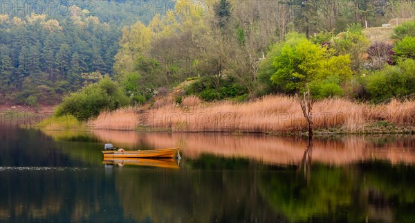 Small yellow metal fishing boat with small engine mount floating peacefully on a lake in South