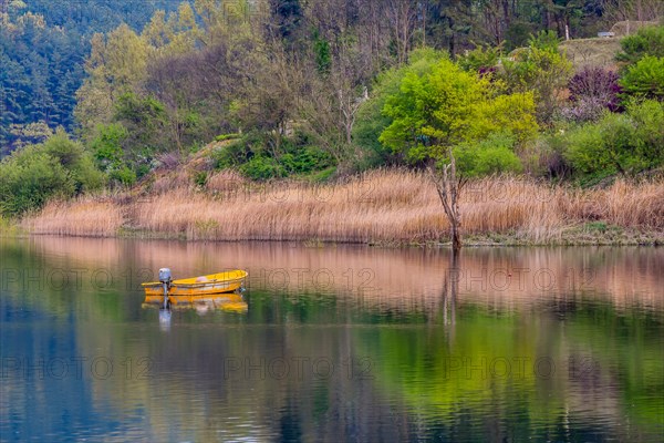 Small yellow metal fishing boat with small engine mount floating peacefully on a lake in South