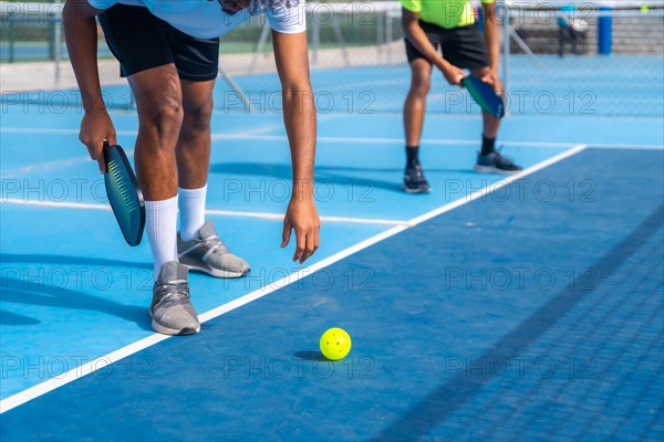 Cropped photo of the lower part of an african man bending to catch a pickleball ball from the floor
