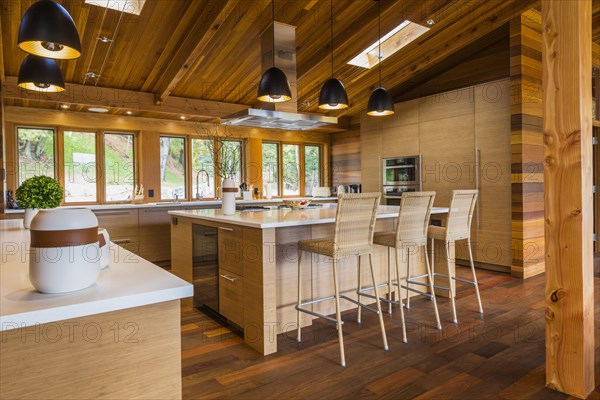 Bamboo wood buffet and island with white quartz countertops and high wicker chairs, cabinets in