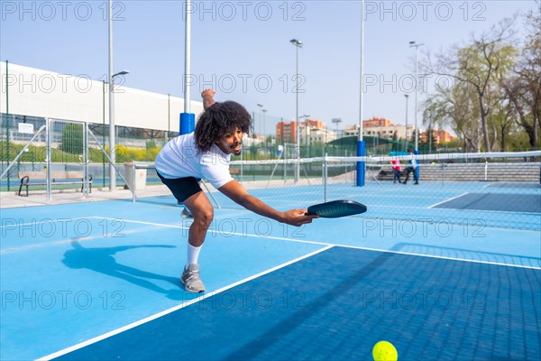 Full length photo of an african sportive man trying to reach the ball playing pickleball in an