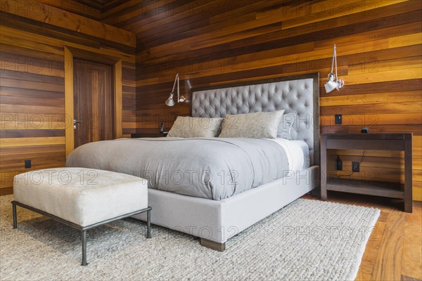 King size bed with grey upholstered panel headboard, ottoman and wooden end tables in master