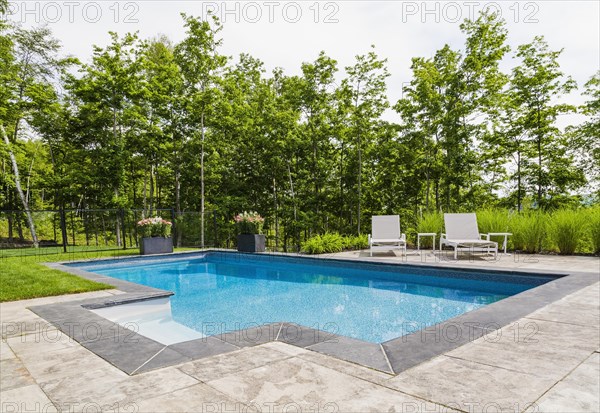Two white long chairs on edge of in-ground swimming pool with flowers in planters in residential