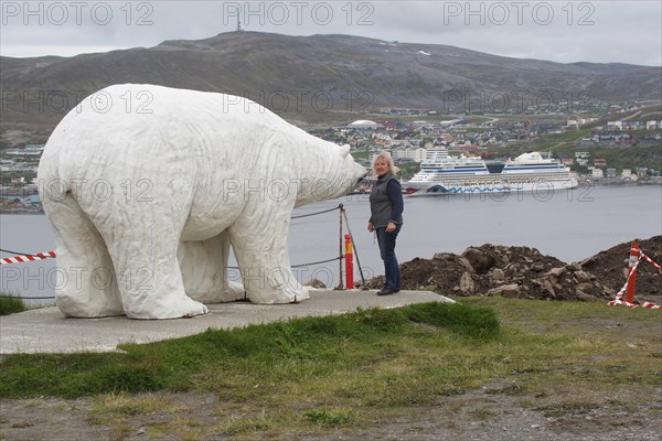 Polar bear sculpture in front of the town of Hammerfest with cruise ship Aida in the harbour,