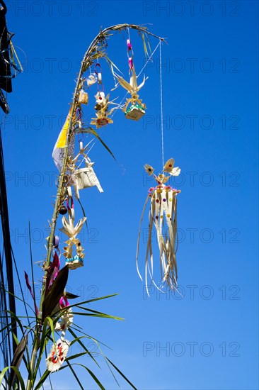Ornate jewellery woven from palm leaves on bamboo poles, on a village street in Amed, Karangasem,