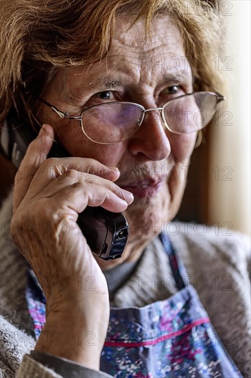Laughing senior citizen with smock talking on the phone at home in her living room, Cologne, North