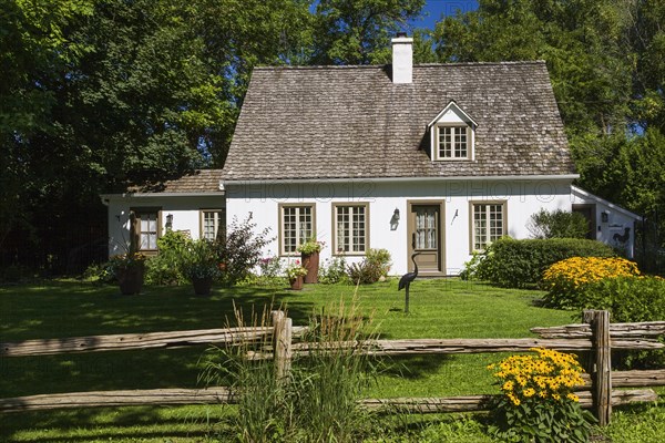 Old circa 1886 white with beige and brown trim Canadiana cottage style home facade with landscaped