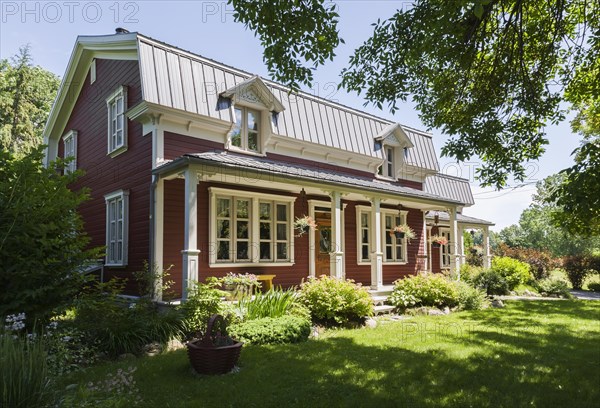 Old 1892 burgundy with white trim pinewood plank house facade with mansarde style grey sheet metal
