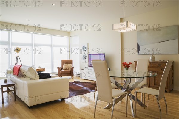 Dining room area with round glass table, white high-back leather chairs and white leather sofa in