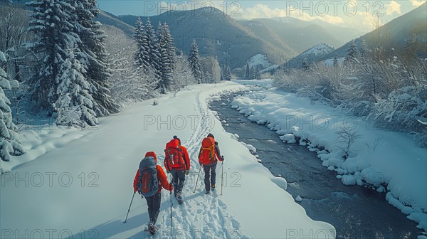 Snowshoers traveling alongside a river in a beautiful snow-covered landscape with winter trees and