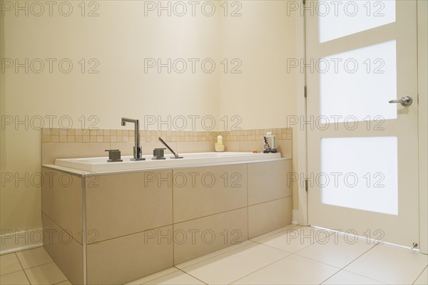 Soaking tub encased in a ceramic tile base in bathroom inside a renovated ground floor apartment in