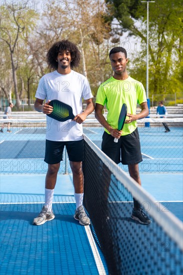 Vertical Portrait of two young african american pickleball players standing looking at camera