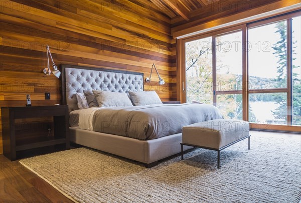 King size bed with grey upholstered panel headboard, ottoman and wooden end tables in master