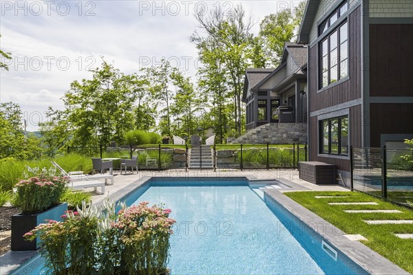 In-ground swimming pool and rear view of contemporary natural stone and brown stained wood and