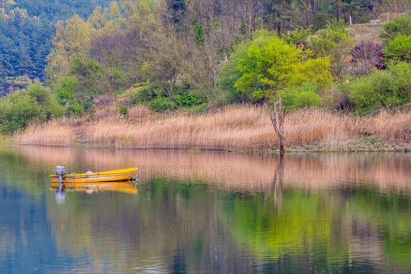 Small yellow metal fishing boat with small engine mount floating peacefully on a lake in South