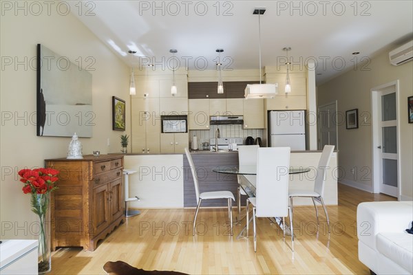 Dining room with round glass table, white leather high -back chairs and kitchen inside a renovated