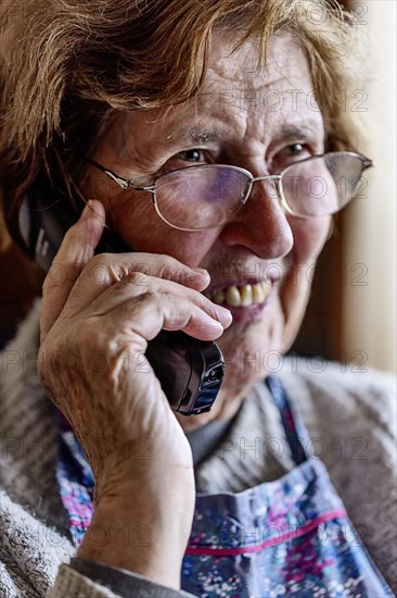 Laughing senior citizen with smock talking on the phone at home in her living room, Cologne, North