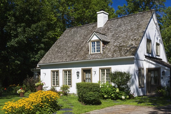 Old circa 1886 white with beige and brown trim Canadiana cottage style home facade with landscaped