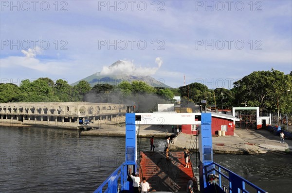 Lake Nicaragua, Ferry on the shore of a lake with an active volcano in the background and cloudy