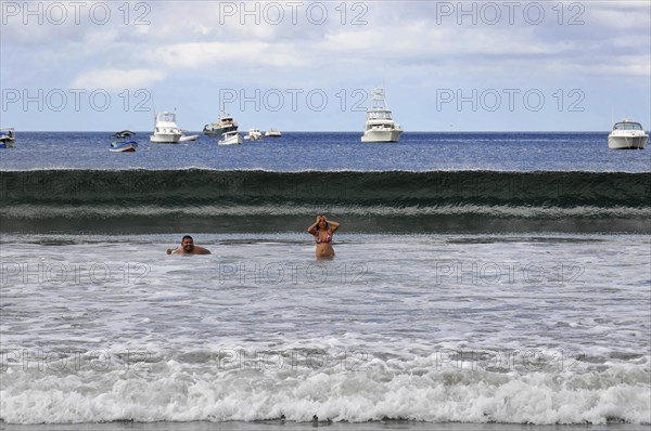 San Juan del Sur, Nicaragua, swimmers in the water in front of a big wave, boats and blue sky in