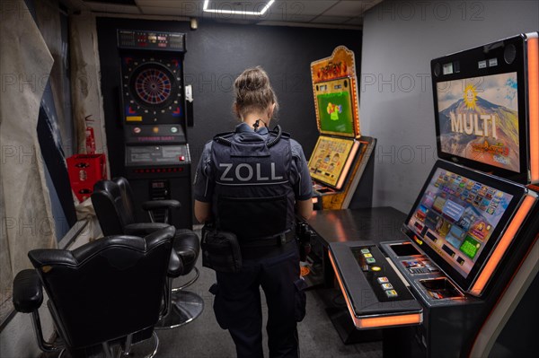 Customs officer looks at slot machines and surveillance equipment in a dark room, The Cologne