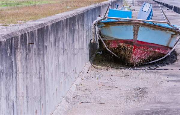 Front view of old dilapidated red, white and blue fishing boat with barnacles on bottom sitting on