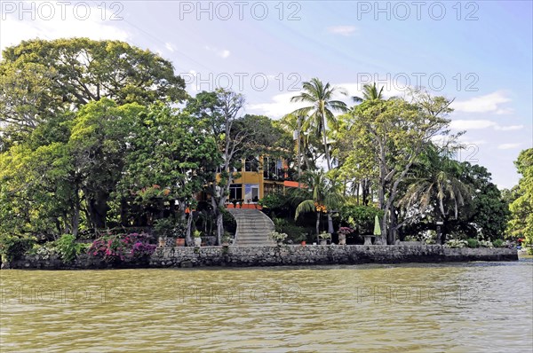 Granada, Nicaragua, Colourful house on the lakeshore with a boat in front, surrounded by palm