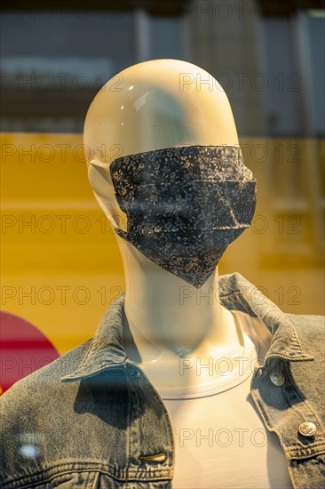 Mannequin with a corona mask on its face in a shop window of a fashion shop in the city centre of