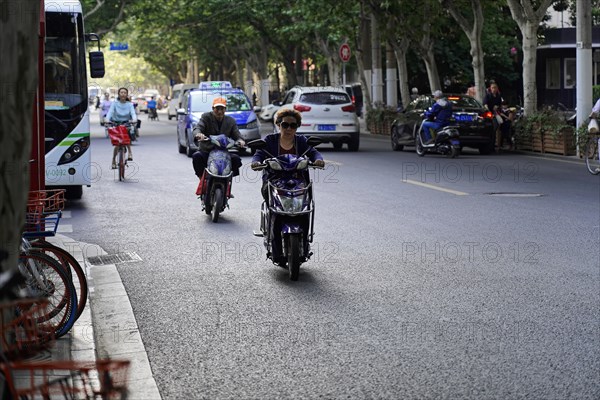 Traffic in Shanghai, Shanghai Shi, people riding scooters and bicycles along a tree-lined street,