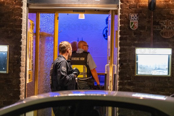 A customs officer enters an illuminated business premises in the evening hours, The Cologne police