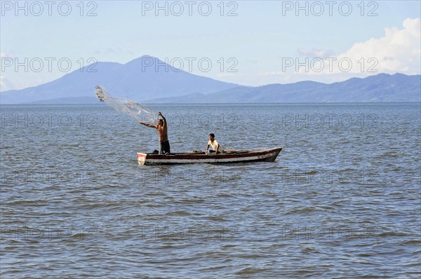 Lake Nicaragua, Two men in a boat casting a fishing net on a lake, mountains in the background,