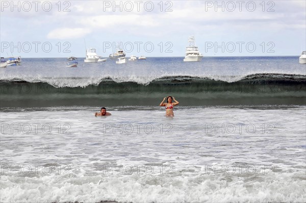 San Juan del Sur, Nicaragua, Swimmers in the sea with a big wave in the background and boats on the
